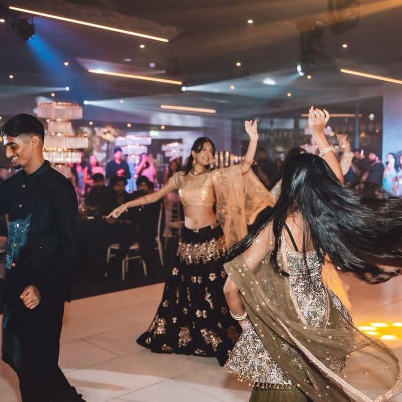 Members dancing in lehengas and formal dress on the floor at a society event.
